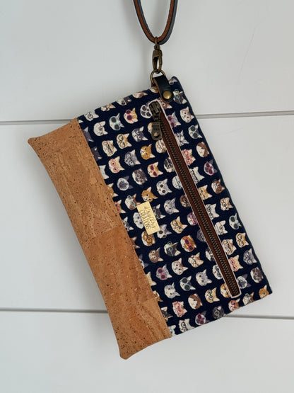 Clutch wallet with cats in glasses. Shows a brown zipper, brass KrisChris tag, and a D ring swivel snap atttached to a wrist strap.